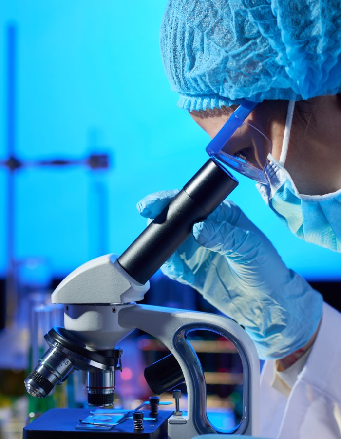 Profile view of concentrated Asian microbiologist examining sample with help of modern microscope while wrapped up in work at dim laboratory